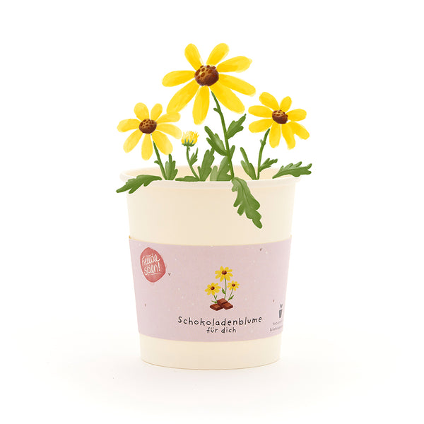 Taza con flores de chocolate amarillo y follaje verde, etiqueta con la inscripción “Flor de chocolate para ti”.