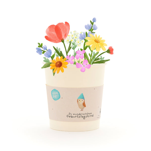 Una maceta con flores de colores y una cinta con la inscripción “Qué hermoso cumpleañero”.