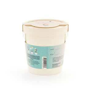 Maceta beige con etiqueta y asa azules, juego de regalo para un prado de flores, etiquetas "de" y "para" visibles.