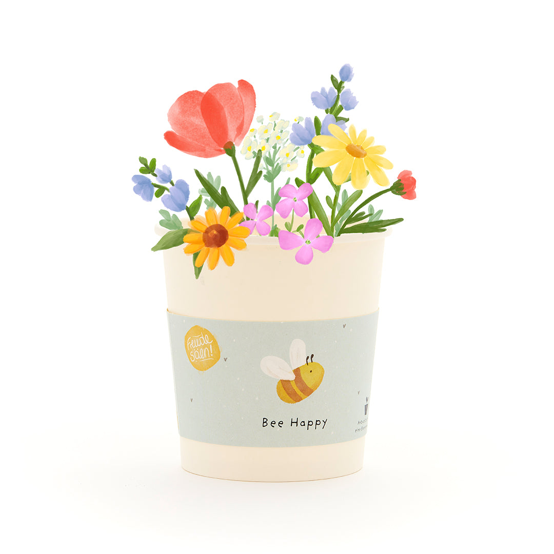 Maceta con flores de colores y una abeja en la etiqueta que dice "Bee Happy".