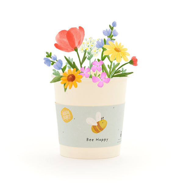 Maceta con flores de colores y una abeja en la etiqueta que dice "Bee Happy".