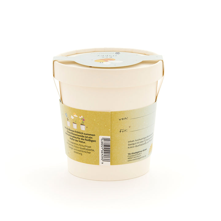 Maceta de color beige con etiqueta verde con texto y pequeñas ilustraciones de flores y abejas.