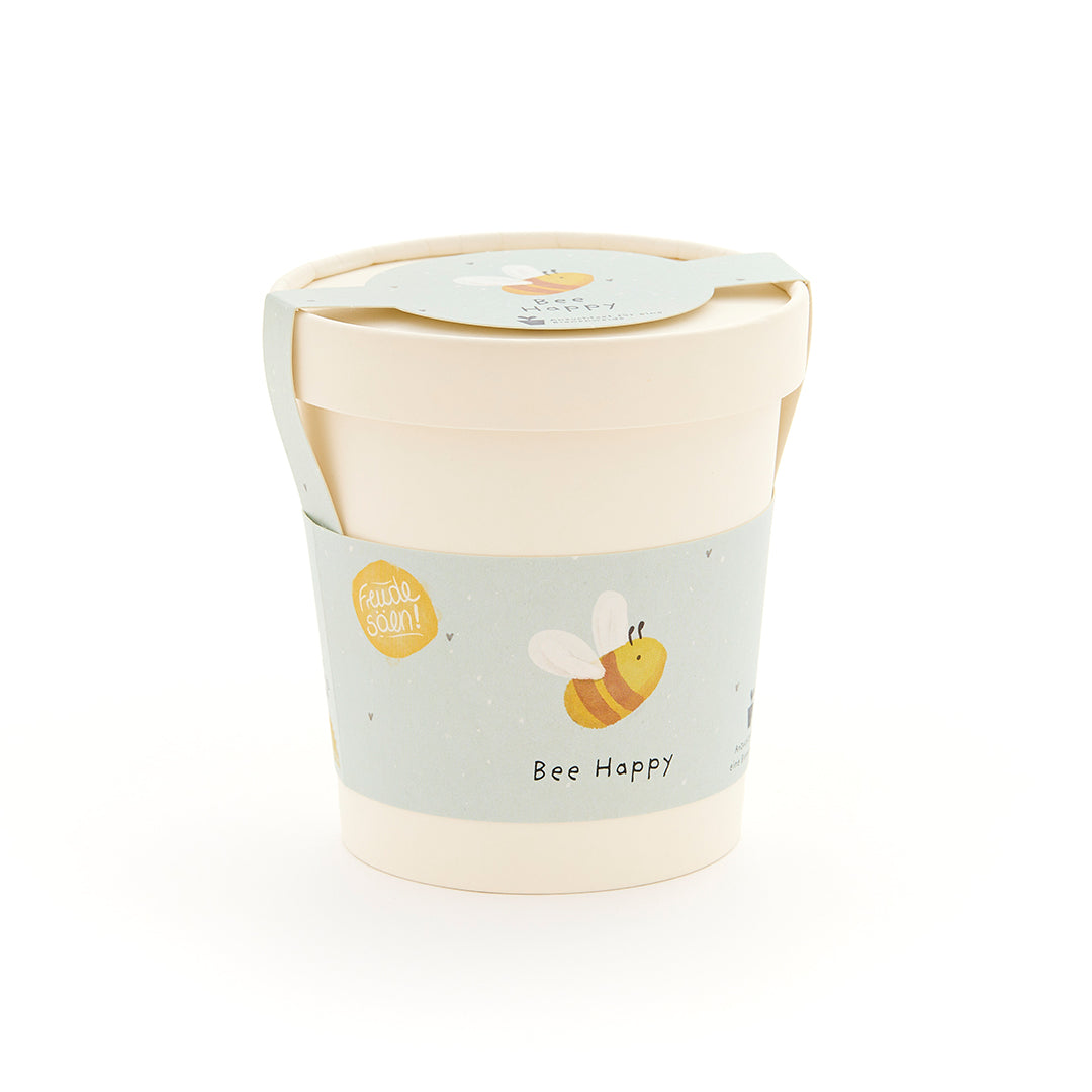 Taza beige con una etiqueta azul claro que presenta una abeja dibujada y las palabras "Bee Happy".