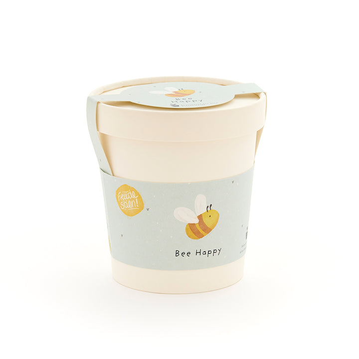 Taza beige con una etiqueta azul claro que presenta una abeja dibujada y las palabras "Bee Happy".