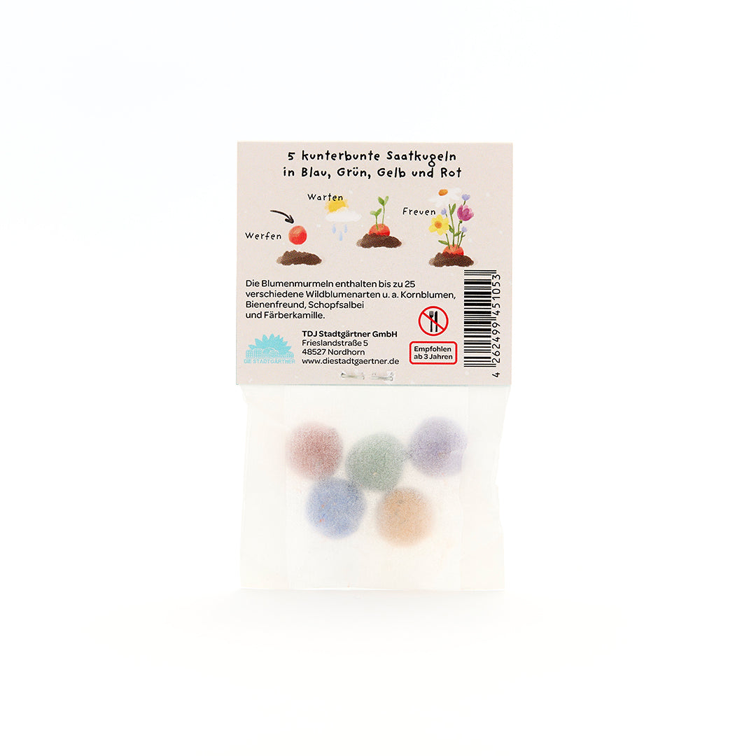 Cinco bolas de semillas de colores en un paquete transparente con instrucciones etiquetadas en alemán.