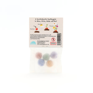 Cinco bolas de semillas de colores en un paquete transparente con instrucciones etiquetadas en alemán.