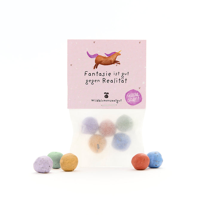 Bolsa con bolitas de semillas de colores y packaging morado con un unicornio y el texto “La imaginación es buena contra la realidad”.