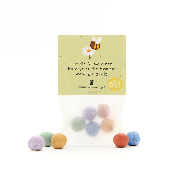 Bolsa con bolitas de semillas de colores y una etiqueta con el dibujo de una abeja y el dicho "Si la flor está doblada, probablemente el abejorro estaba demasiado gordo".
