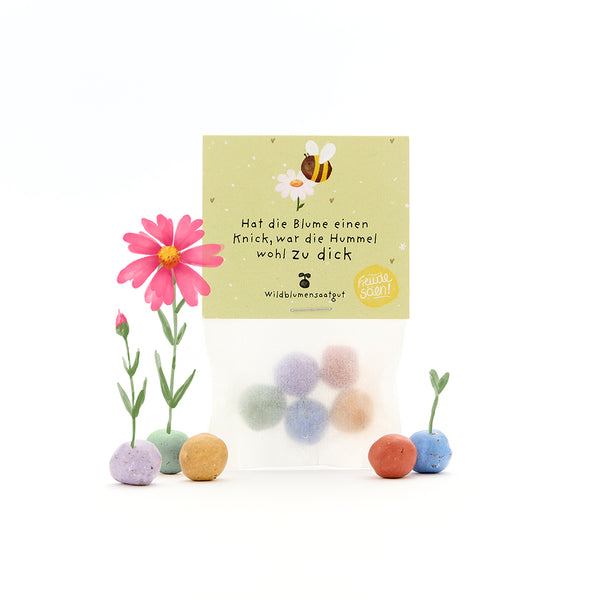Una bolsa con bolas de semillas de colores, algunas flores florecientes y una etiqueta con una abeja y el dicho: "Si la flor está doblada, el abejorro probablemente estaba demasiado gordo".