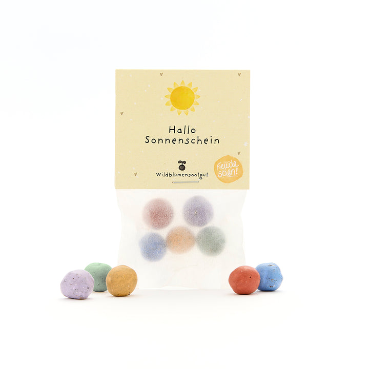 Bolsa con bolitas de semillas de colores y etiqueta “Hello Sunshine”, además de un sol y pequeños corazones, semillas de flores silvestres.