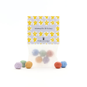 Bolsa de bolas de semillas de colores, etiqueta con estrellas amarillas y las palabras “Namaste Bitches” y “Wildflower Seeds”.