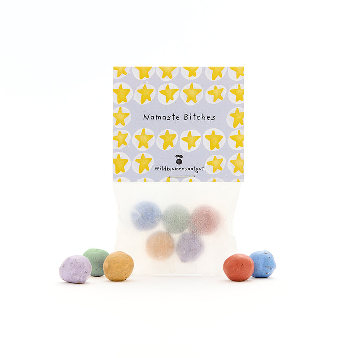 Bolsa de bolas de semillas de colores, etiqueta con estrellas amarillas y las palabras “Namaste Bitches” y “Wildflower Seeds”.