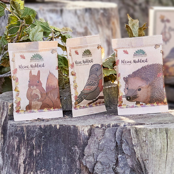 Tres paquetes de comida para mascotas con imágenes de una ardilla, un pájaro y un erizo en troncos de árboles.