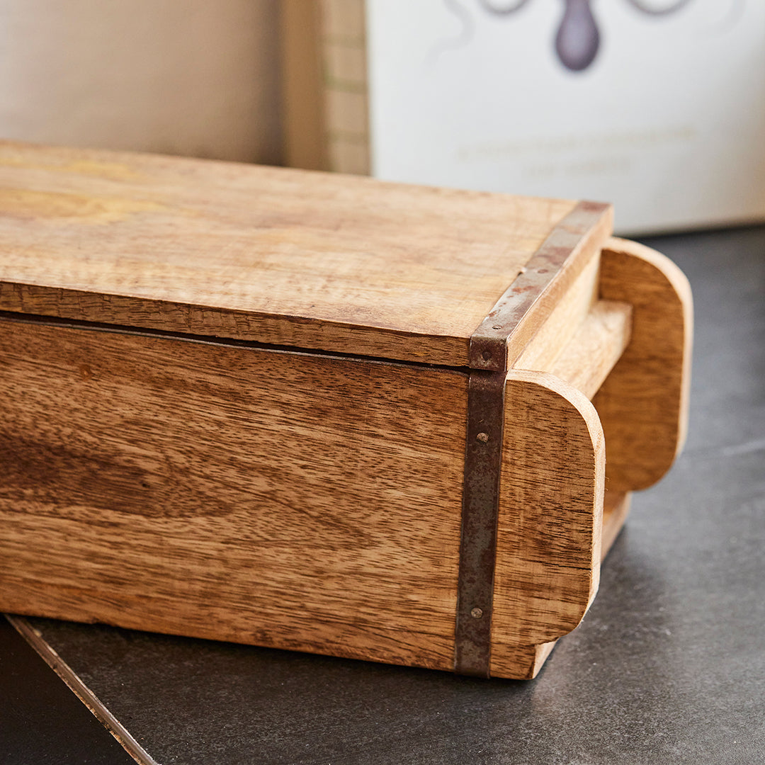 Caja rectangular de madera con refuerzos metálicos sobre superficie oscura.