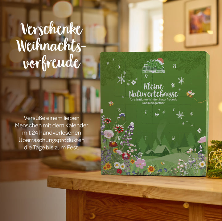 Sobre una mesa de madera, delante de una estantería, se encuentra un calendario de Adviento verde con motivos florales y junto a él se puede leer: "Regala la ilusión de la Navidad".