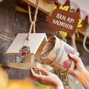Una persona llena una pajarera de madera con alpiste de una bolsa de papel; en la imagen se lee "Ideal para rellenar".