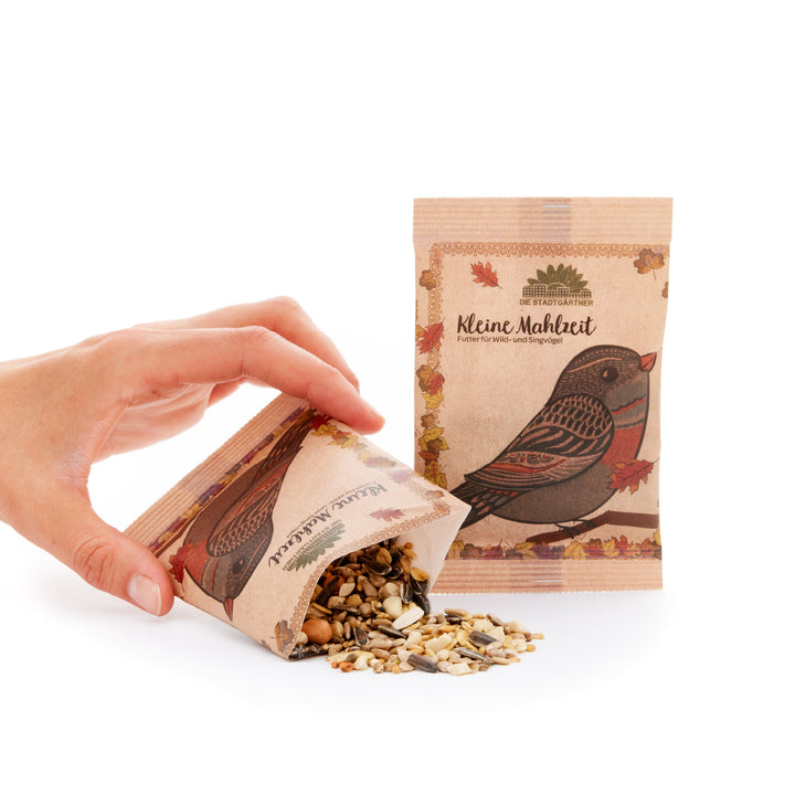 Mano vertiendo semillas para pájaros de una bolsa de papel marrón con un motivo de pájaro y la inscripción "Small Meal" al lado de una bolsa vertical sin abrir.