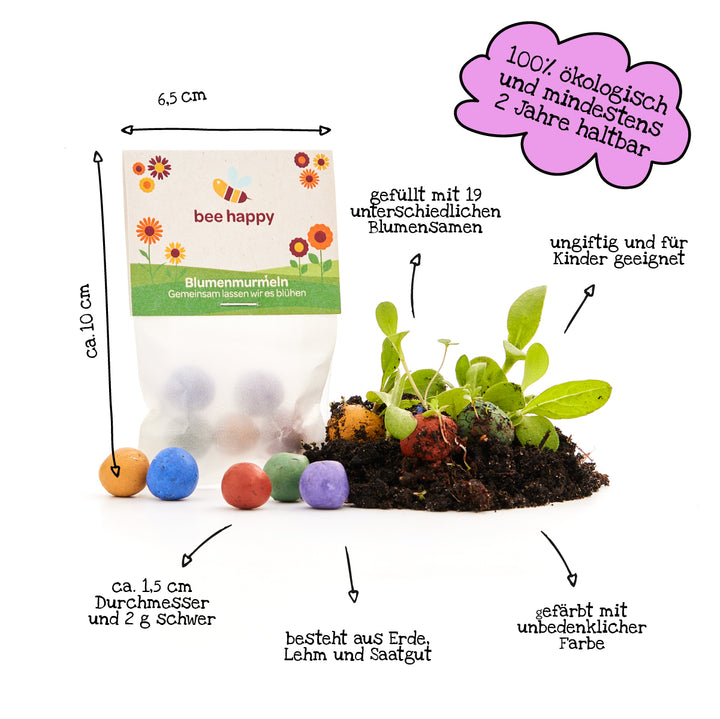 Una bolsa de canicas de semillas de flores de varios colores, junto a tierra con plantas en germinación; etiquetada con información sobre tamaño, composición y respeto al medio ambiente.