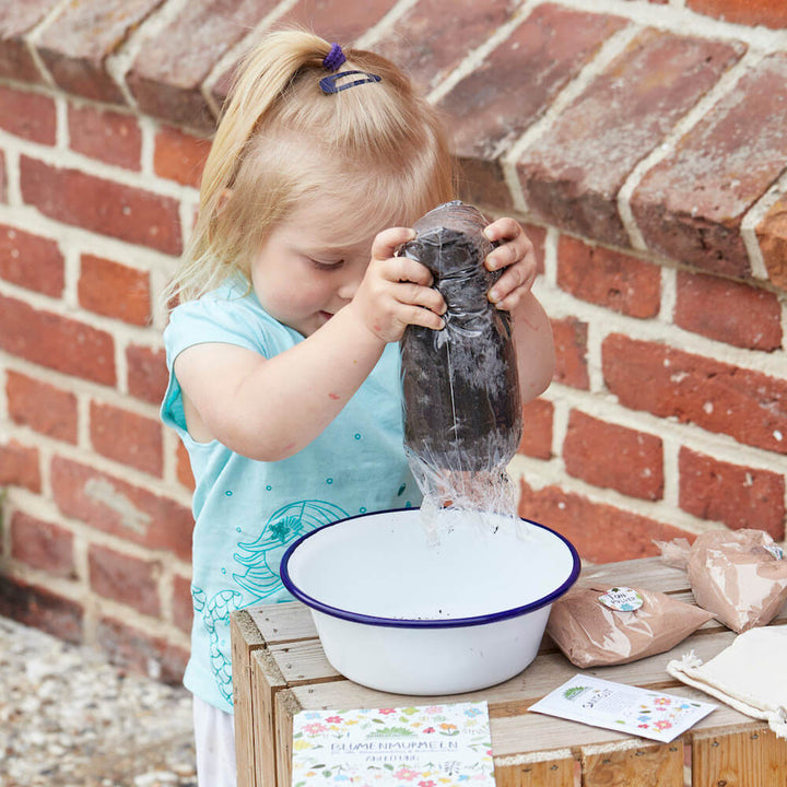Niña vertiendo agua de una botella en un recipiente mientras trabaja en el jardín.