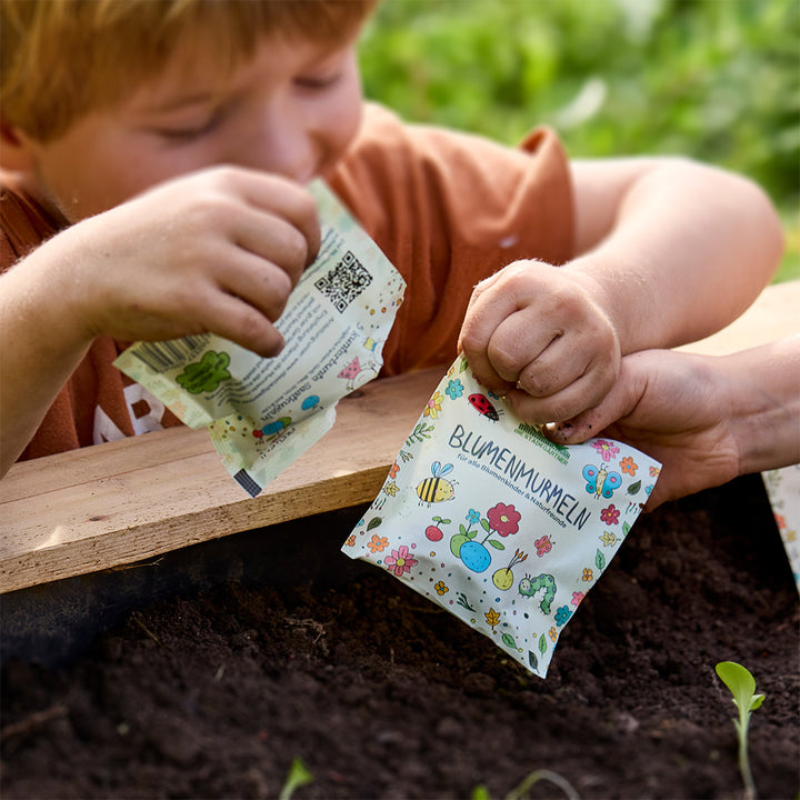 Un niño sostiene una bolsa colorida con una etiqueta que dice “canica de flores” sobre un lecho de tierra.