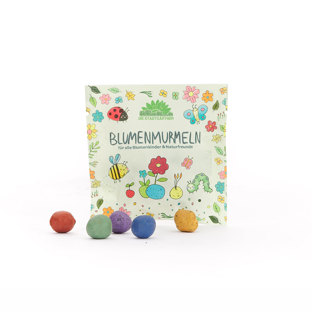 Paquete con la inscripción “Flower Marbles” y bolas redondas de colores en el frente; el embalaje está ilustrado con flores de colores, insectos y animales.