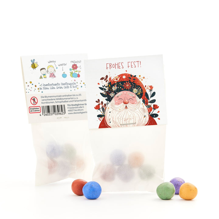 Una bolsa de bolas de semillas de colores, delante una tarjeta con un dibujo de Papá Noel y las palabras "¡Feliz Navidad!"