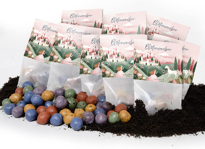 Varias bolsas etiquetadas como “Blütenzauber” (Magia de flores) con un diseño de cuento de hadas, con coloridas bombas de semillas tiradas en el suelo frente a ellas.
