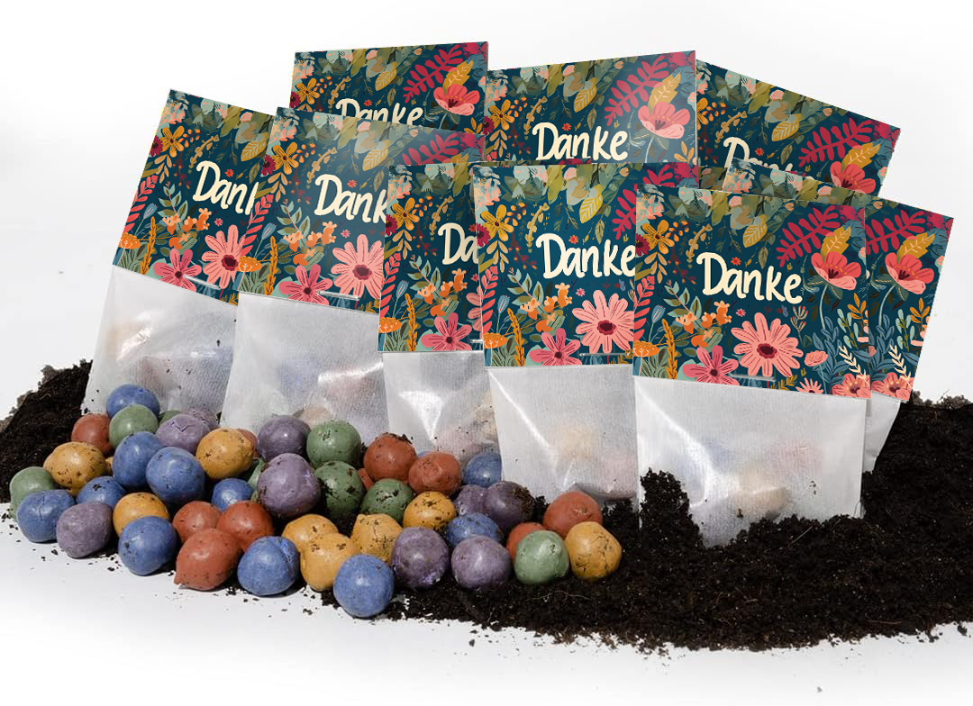 Varias bolsas de colores con la palabra "Gracias" y patrones florales se encuentran sobre el suelo, con bolas de semillas de colores frente a ellas.