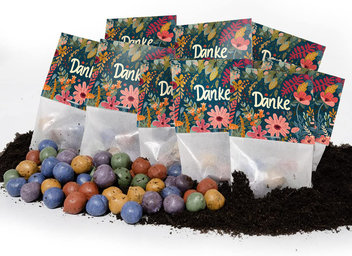Varias bolsas de colores con la palabra "Gracias" y patrones florales se encuentran sobre el suelo, con bolas de semillas de colores frente a ellas.