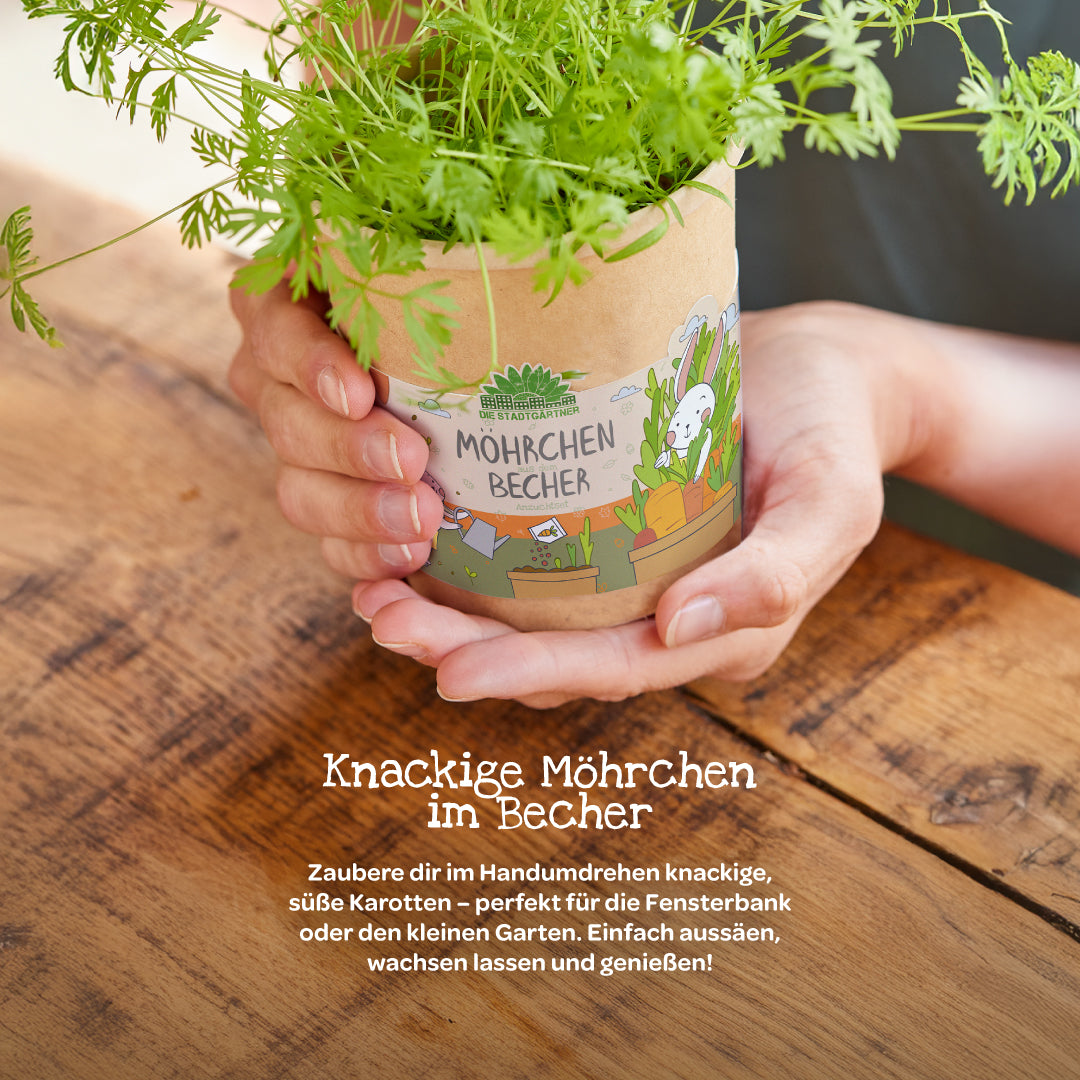 Persona sosteniendo una taza con plantas de zanahoria creciendo sobre una mesa de madera, etiqueta "Taza de zanahoria".