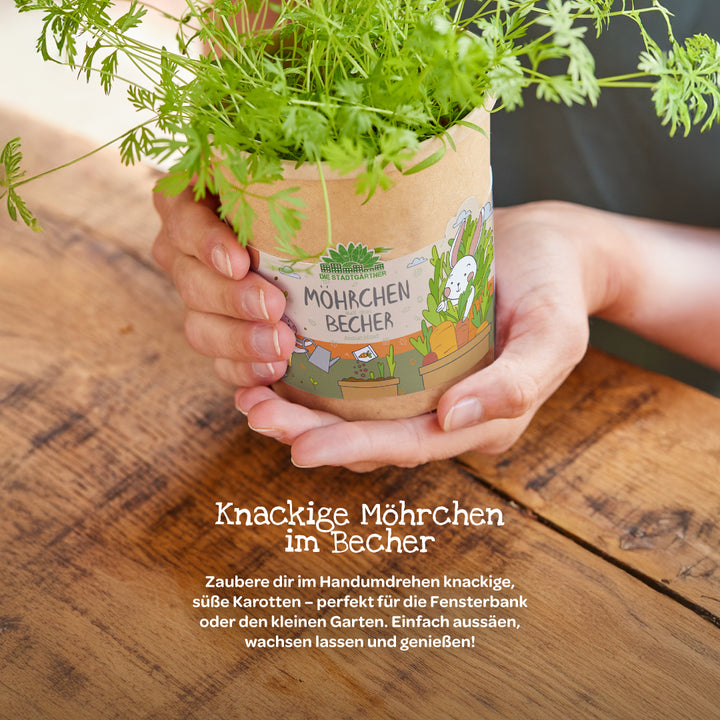 Persona sosteniendo una taza con plantas de zanahoria creciendo sobre una mesa de madera, etiqueta "Taza de zanahoria".