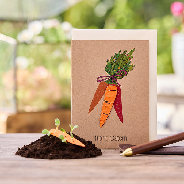 Tarjeta de Pascua con motivo de zanahoria y la inscripción "Felices Pascuas", al lado un pequeño montículo de tierra con zanahorias y brotes.