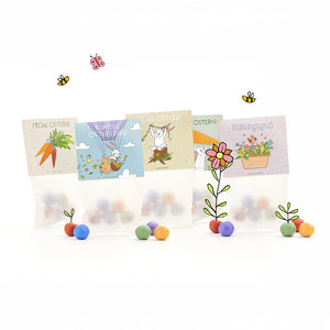 Cuatro bolsas de Pascua con bolas de colores, cada una con alegres motivos ilustrados de Pascua y primavera y saludos en alemán como "Felices Pascuas" y "Saludos de primavera", rodeadas de flores, abejas y mariposas dibujadas.