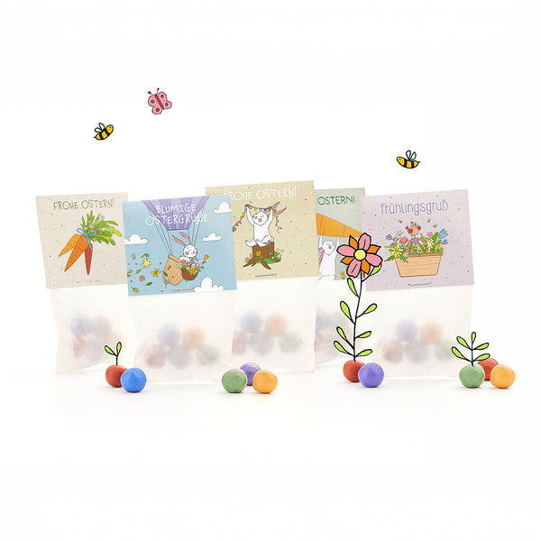 Cuatro bolsas de Pascua con bolas de colores, cada una con alegres motivos ilustrados de Pascua y primavera y saludos en alemán como "Felices Pascuas" y "Saludos de primavera", rodeadas de flores, abejas y mariposas dibujadas.