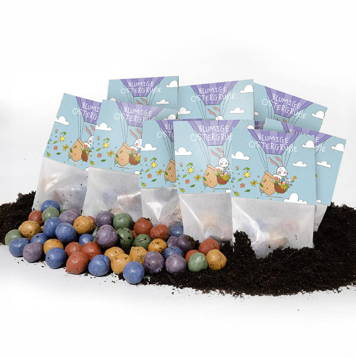 Varias bolsitas con la inscripción "Felices Pascuas con flores" y un motivo de conejito de Pascua, delante de las cuales hay bombas de semillas de colores en el suelo.