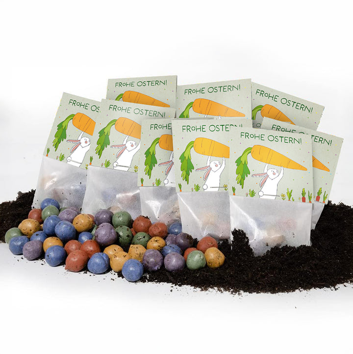 Varios paquetes de semillas de Pascua con la inscripción "¡Felices Pascuas!" y confeti de semillas de colores en la tierra.