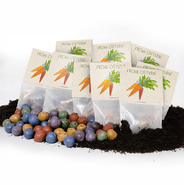 Varias bolsitas con la inscripción “¡Felices Pascuas!” y un dibujo de una zanahoria, delante de ellas bolas de semillas de colores y tierra.
