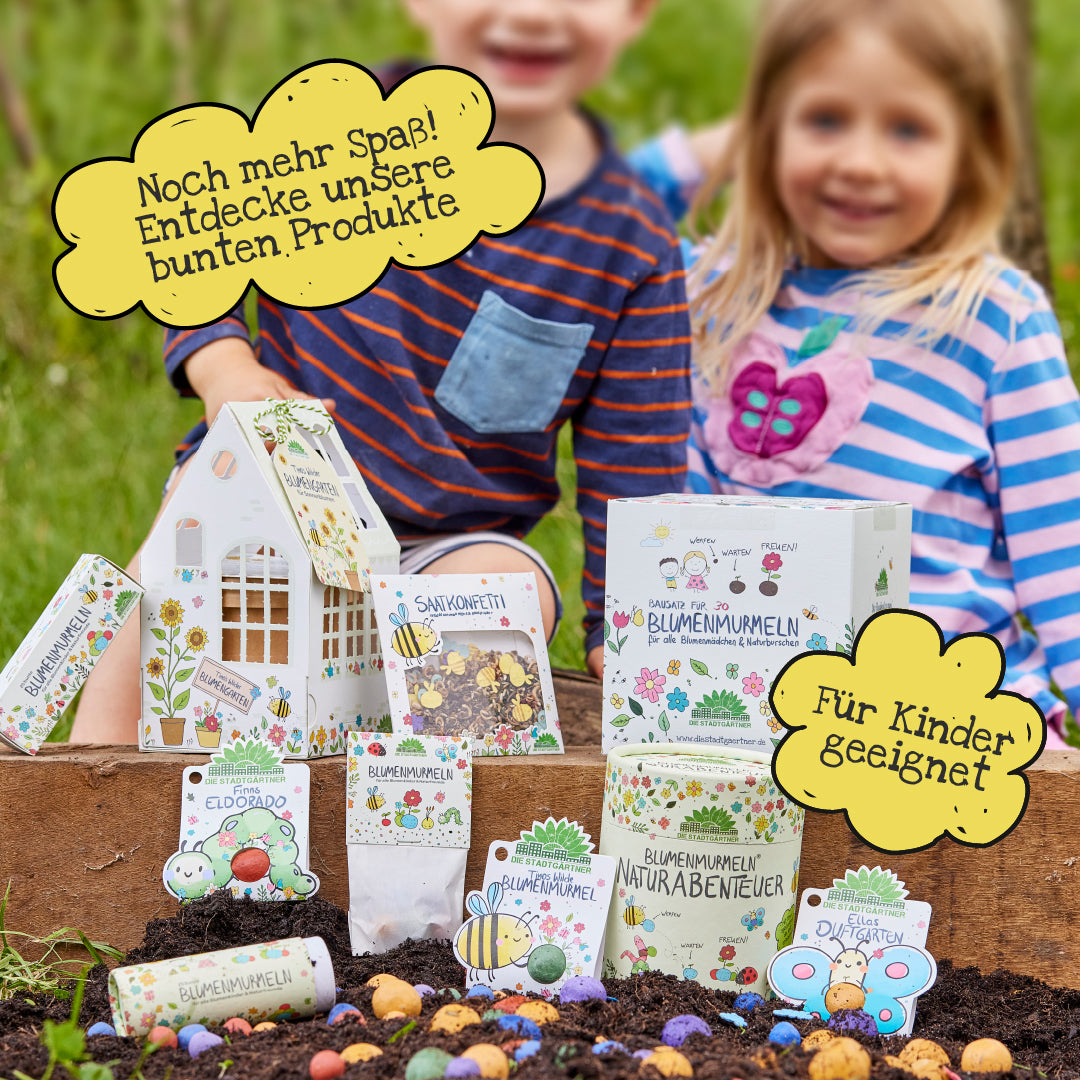 Dos niños se sientan en el jardín detrás de una selección de productos de semillas de flores y envases coloridos y aptos para niños que promueven aventuras en la naturaleza y juegos creativos.