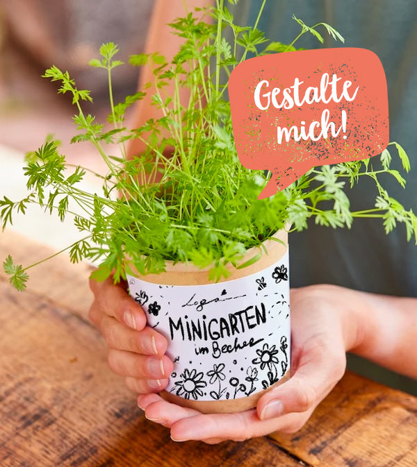 Persona sosteniendo una taza con una planta de hierbas que dice "Mini jardín en una taza" y "¡Diséñame!"