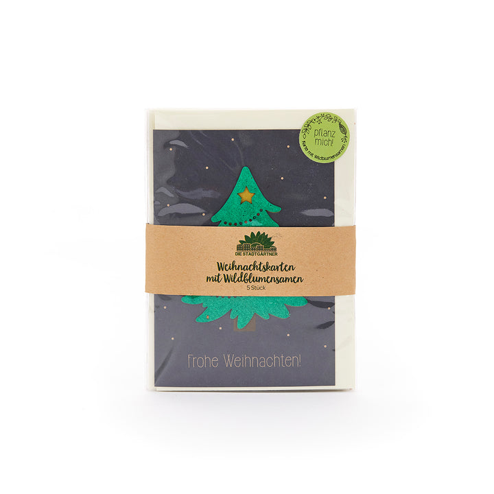 Tarjeta de Navidad con un árbol de Navidad verde y una estrella, en un paquete con una cinta de papel marrón y la inscripción "Tarjetas de Navidad con semillas de flores silvestres", al lado una pegatina verde con "Plántame".