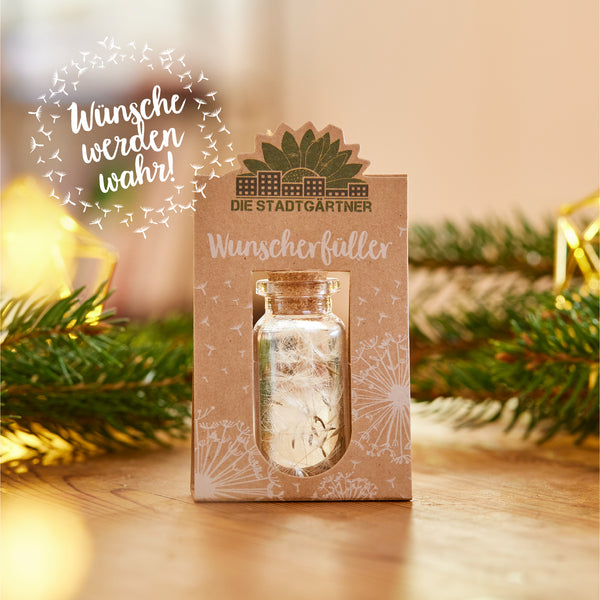 Una pequeña botella de vidrio con corcho en un paquete con la etiqueta "Los jardineros de la ciudad cumplen los deseos" junto a ramas de abeto y adornos navideños.