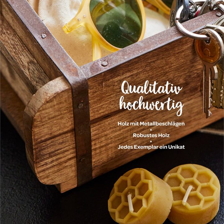 Caja de madera con herrajes metálicos, gafas de sol, un juego de llaves y dos velas de cera de abejas; texto: "Alta calidad: madera con herrajes metálicos, madera robusta, cada pieza es única".