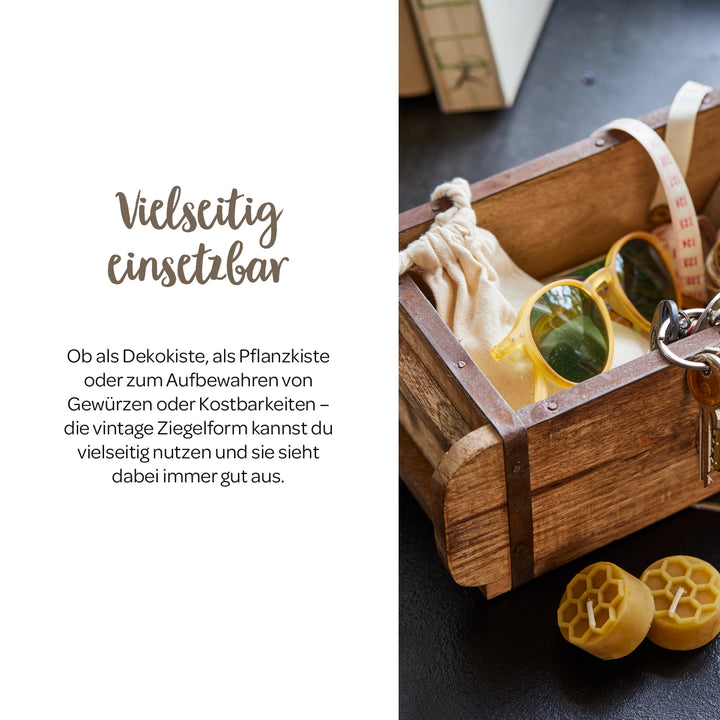 Caja de madera de estilo vintage con gafas de sol, llaves, bolsa de tela y cinta métrica sobre una mesa, junto a dos bloques de cera amarilla.
