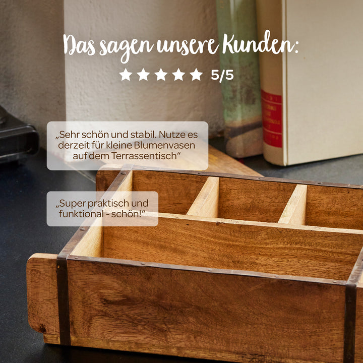 Sobre una mesa hay una caja de madera con compartimentos, al fondo hay libros; encima hay opiniones de clientes en alemán y cinco estrellas con una calificación de 5/5.