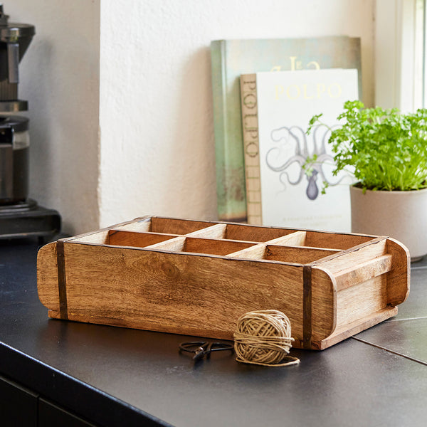 Caja de madera sobre una encimera con una bola de hilo y una planta al fondo.