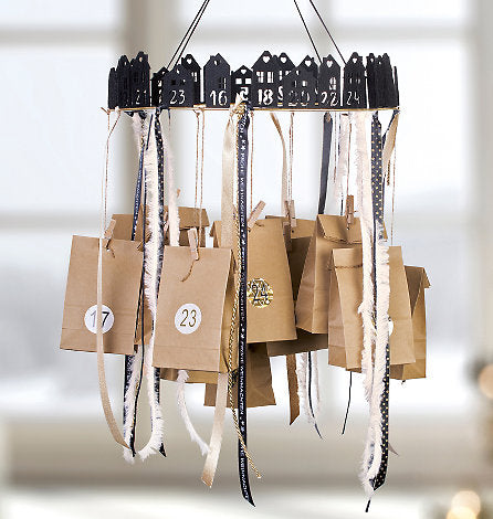 Calendario de Adviento casero elaborado con bolsas de papel marrón colgadas en un marco redondo con casas negras y cintas.