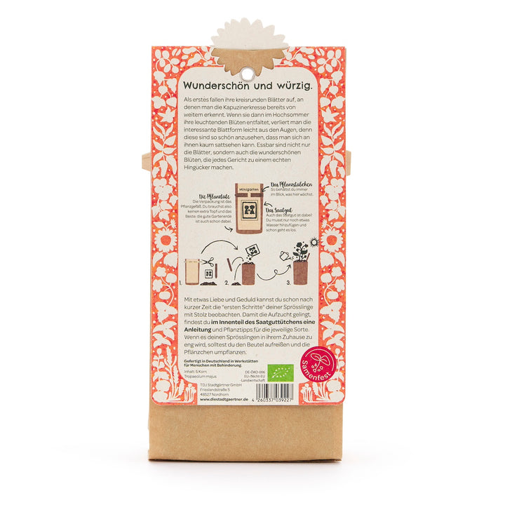Reverso de un paquete de semillas con descripción en alemán, ilustraciones de siembra y un patrón floral naranja y blanco.
