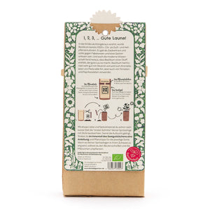 Parte posterior de un paquete con instrucciones en alemán para cultivar albahaca, borde verde decorativo y descripción de texto.