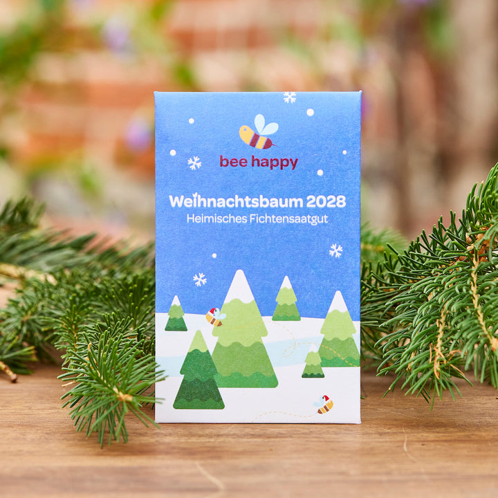 Pack con la inscripción “Árbol de Navidad 2028 Semilla de Abeto Nativo” y un colorido diseño de abeja y abeto, decorado con ramas de abeto en primer plano.
