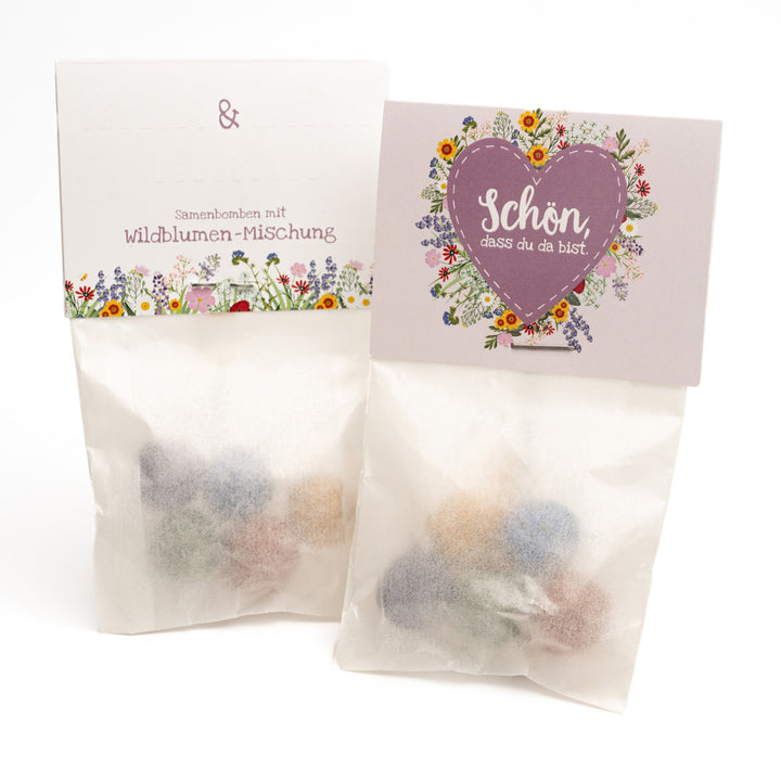 Dos bolsas de bombas de semillas de flores silvestres, decoradas con motivos florales y un corazón con la inscripción "Es genial que estés aquí".
